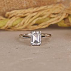 an emerald - cut diamond ring sits on a table next to a woven baguette