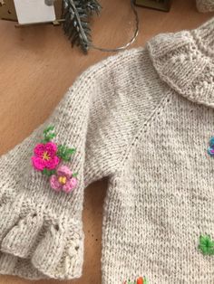 a knitted sweater with flowers on it sitting on a table next to a christmas tree