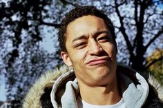 a close up of a person wearing a jacket and looking at the camera with trees in the background