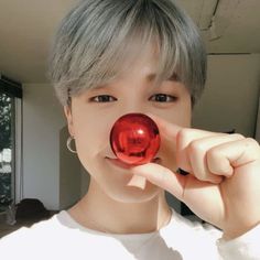 a person with grey hair holding a red ball in front of their face and looking at the camera