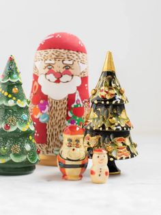 three small christmas trees are next to a santa clause and other holiday decorations on a white surface