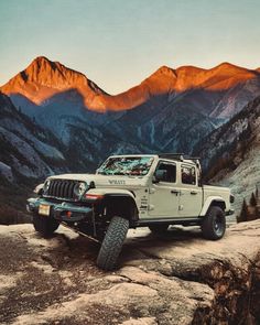 a white jeep parked on top of a rocky hill with mountains in the back ground