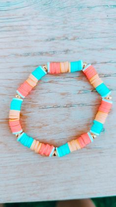 a bracelet made out of colorful beads on top of a wooden table next to a person's hand