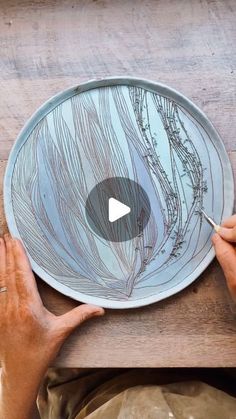 two hands are holding a plate that has been painted with blue and white swirls