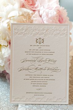 the wedding card is next to some pink and white peonies on a lace tablecloth