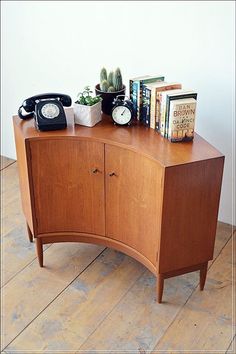 a wooden cabinet with books and an alarm clock on it's side, next to a phone