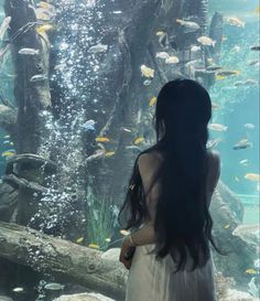 a woman standing in front of an aquarium looking at fish