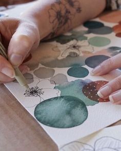 a woman is drawing on paper with a pencil and watercolor pen while sitting at a table