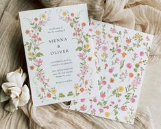 two wedding cards with flowers on them sitting next to a flowery cloth and tulle