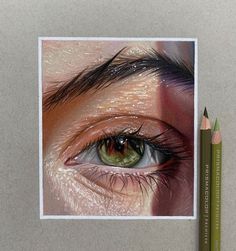 a pencil drawing of an eye with long lashes and green eyeshade next to two colored pencils