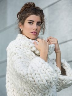 a woman wearing a white knitted sweater posing for the camera with her hands on her hips