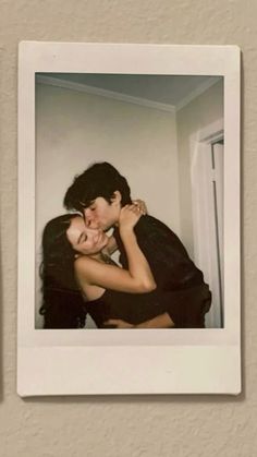 a man and woman embracing each other in front of a wall mounted polaroid frame