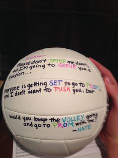 a white volleyball with writing on it in someone's hand, next to a piece of paper