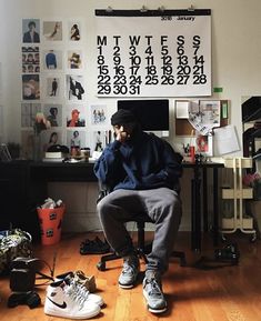 a man sitting on top of a wooden floor in front of a wall covered with pictures