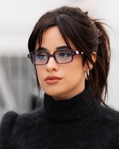 a close up of a person wearing glasses and a black turtle neck sweater with her hair in a pony tail