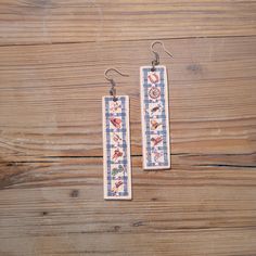 two wooden earrings with designs on them sitting on a wood table next to a pair of scissors