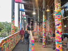 two people walking down a walkway covered in brightly colored ribbons and paper mache sculptures