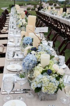 a long table is set with white and blue flowers, candles, and place settings