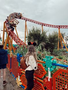 a woman standing in front of an amusement park roller coaster with mickey mouse on it