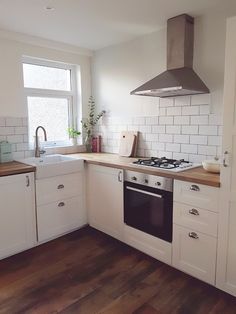 a kitchen with white cabinets and wooden floors, an oven hood over the stove is mounted above the sink