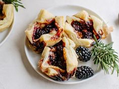 blackberry pies on a plate with fresh berries and rosemary sprigs next to them