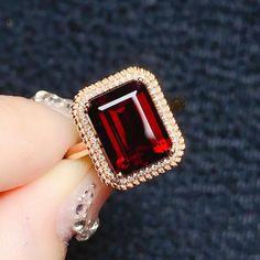 a close up of a person's hand holding a ring with a red stone