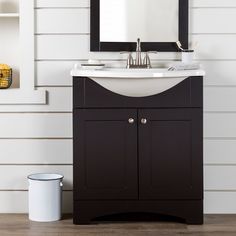 a bathroom vanity with a mirror above it and a trash can next to the sink