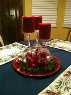 two candles are sitting on top of a red plate with christmas decorations and baubles