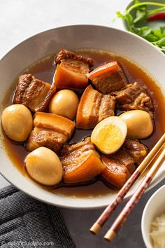 a white bowl filled with beef and potatoes next to chopsticks on a table