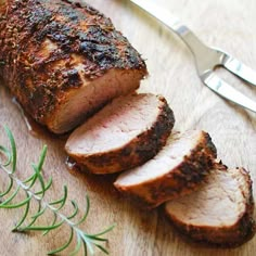 sliced meat sitting on top of a wooden cutting board next to a knife and fork