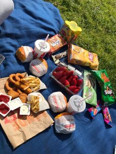 some food is laying out on a blue blanket in the grass with other snacks and condiments