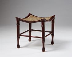 a wooden stool with caned seat and foot rests on a white surface, against a gray background