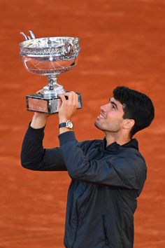 a man holding up a trophy on top of a tennis court