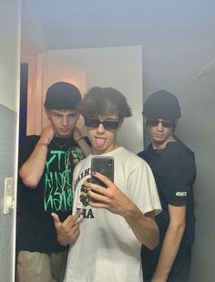 three young men standing in front of a mirror taking a selfie with their cell phone