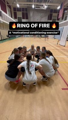 a group of girls huddle together in the middle of a gym floor for a ring of fire