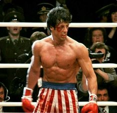 a man with no shirt standing in front of a boxing ring wearing red, white and blue shorts