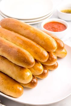 several hot dogs on a plate with dipping sauces in the bowl behind them,