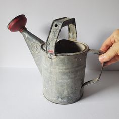 an old watering can being held by a person's hand with a red handle