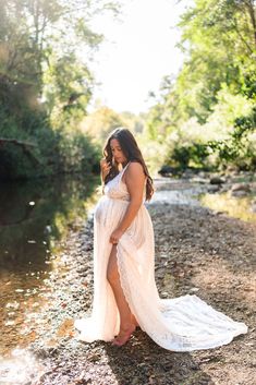 a pregnant woman in a white dress standing on the side of a river