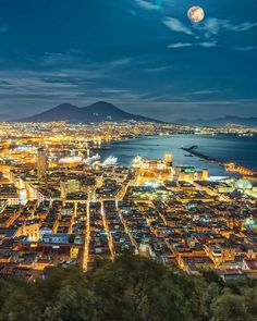 an aerial view of a city at night with the moon in the sky above it