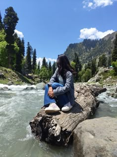 a woman sitting on top of a rock next to a river