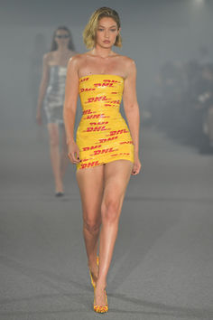 a model walks down the runway in a yellow mini dress with red letters on it