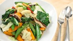 a white bowl filled with vegetables on top of a table next to a fork and knife