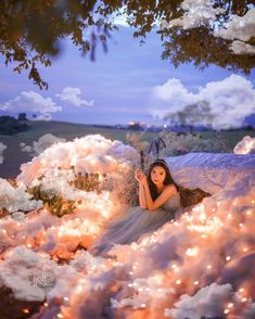 a woman laying on top of a bed covered in white fluffy clouds next to a tree