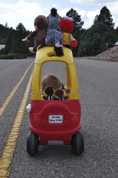 two stuffed animals are sitting on top of a toy car in the middle of the road