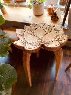 a wooden stool with a flower design on it's seat and some potted plants in the background