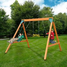 two children playing on a wooden swing set in the grass with trees and blue sky behind them