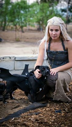 a woman kneeling down next to a black dog