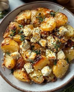 a white plate topped with potatoes covered in feta cheese and herbs on top of a table