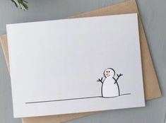 a white card with a snowman drawn on the front and bottom, sitting next to a plant